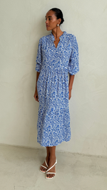 blue and white floral-patterned midi dress with a collared neckline and three-quarter sleeves, styled with white strappy heeled sandals