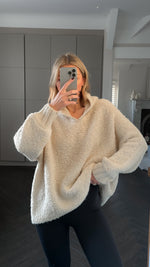 Woman wearing an oversized cream-colored textured knit sweater with a V-neckline, paired with black leggings