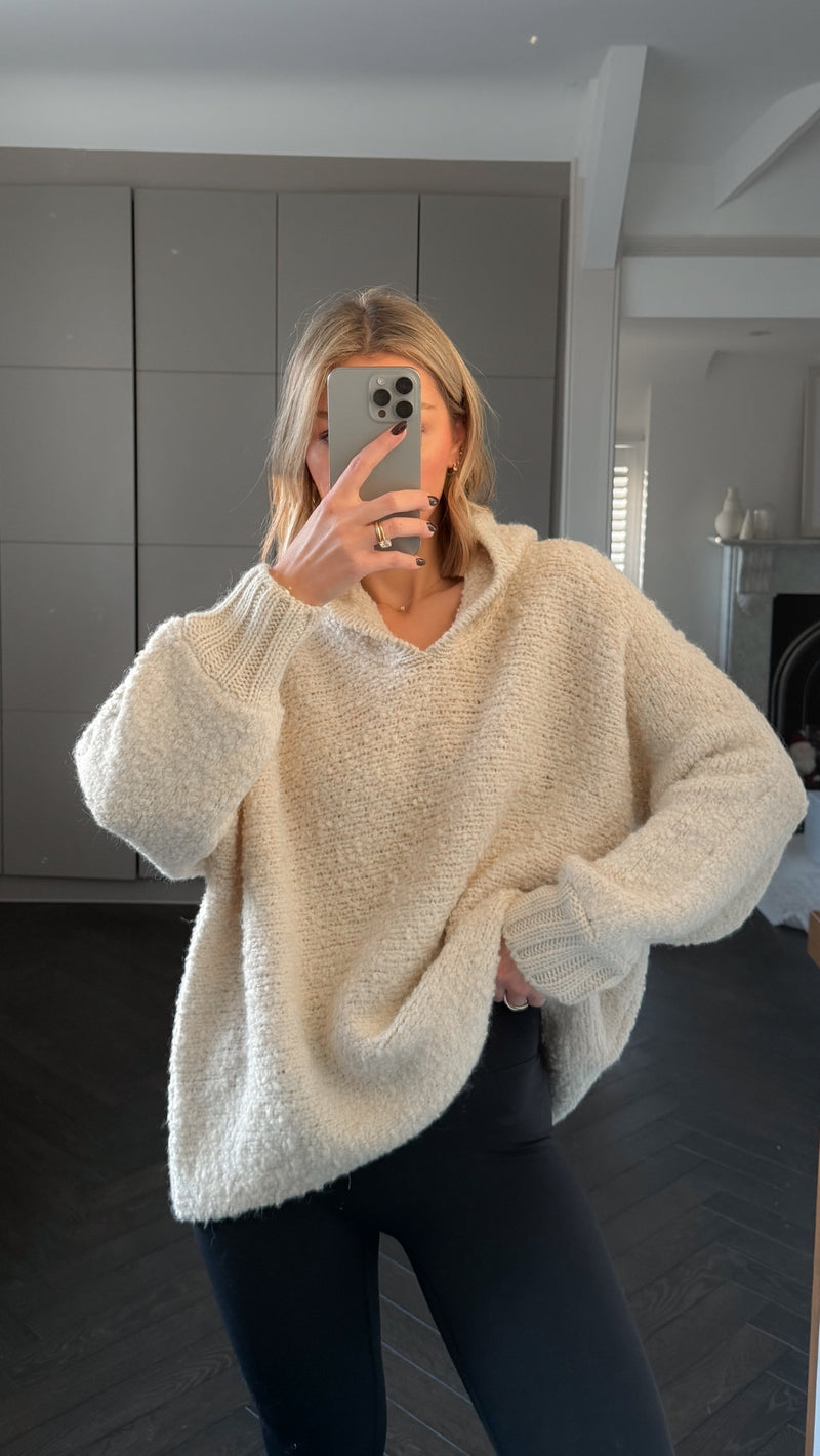 Woman wearing an oversized cream-colored textured knit sweater with a V-neckline, paired with black leggings