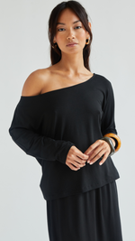 off-shoulder black long-sleeve top paired with a matching black skirt, styled with gold hoop earrings and bracelets