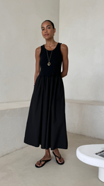 sleeveless black midi dress with a fitted bodice and a flowy skirt, styled with black flip-flops, gold hoop earrings, and a gold pendant necklace