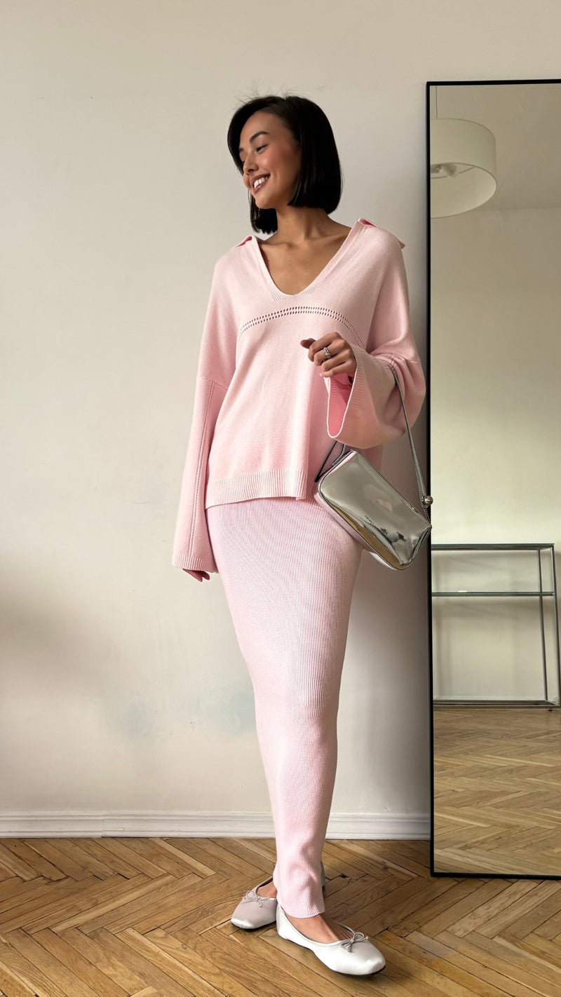 light pink knit set featuring a V-neck sweater with flared sleeves and a matching midi skirt, styled with white ballet flats and a silver metallic crossbody bag