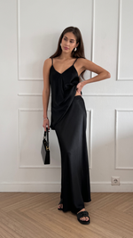 sleek black satin camisole paired with a matching long satin skirt, holding a black handbag