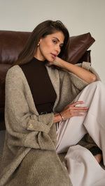 taupe knit cardigan with buttoned cuffs, layered over a dark brown turtleneck top, and paired with cream wide-leg trousers