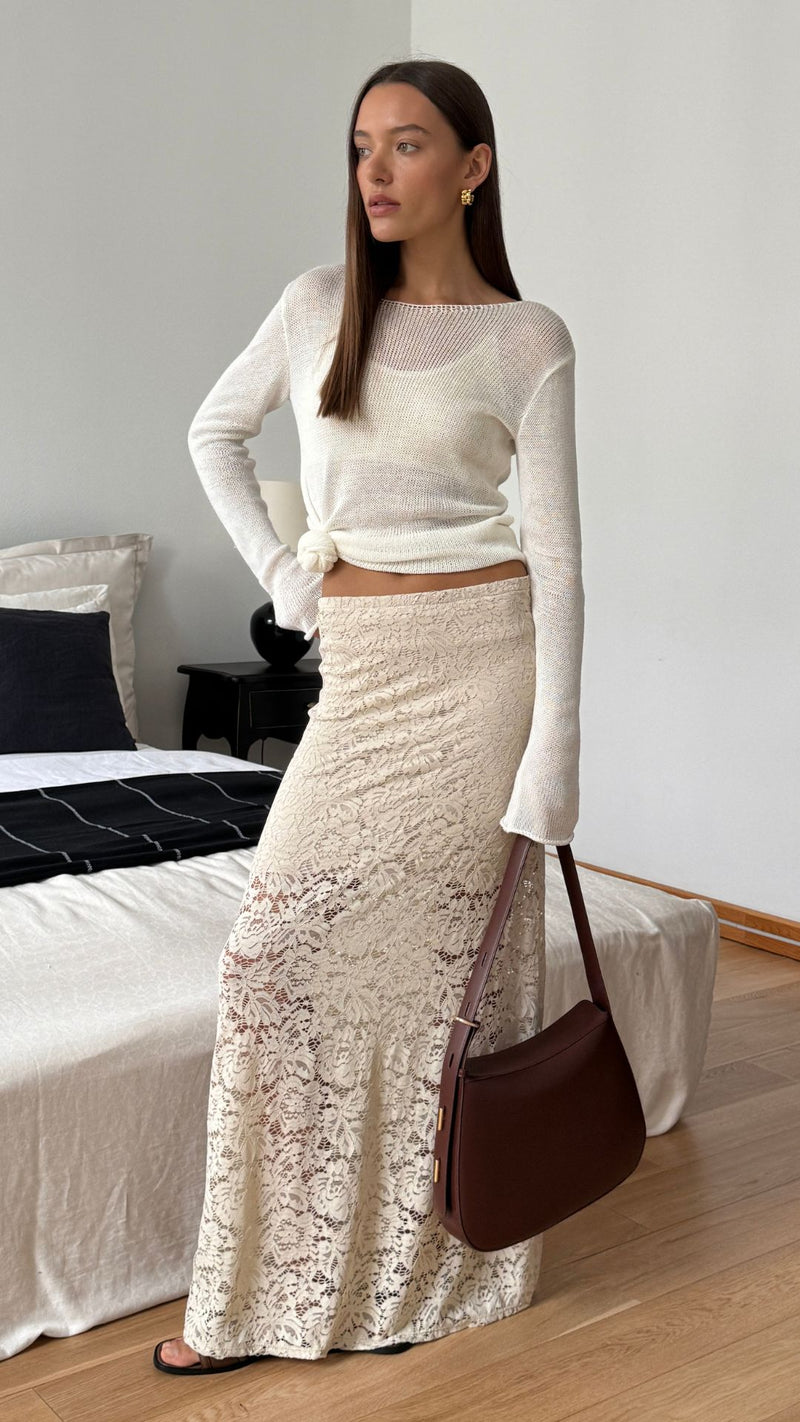 ivory knit top knotted at the waist, paired with a cream lace maxi skirt, accessorized with gold earrings and a brown leather shoulder bag