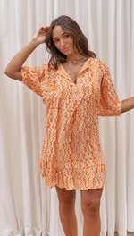 orange and white zigzag-patterned mini dress with a ruffled hem and loose sleeves, accessorized with a gold necklace